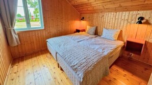 A bedroom with a wooden ceiling, a bed with a quilt, a nightstand, a lamp, and a window with curtains.
