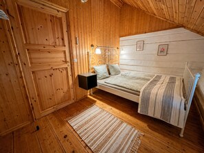 A wooden room with a bed, a nightstand, and a wall-mounted lamp.