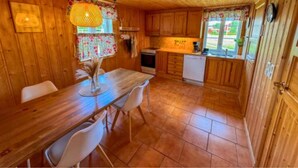 A wooden interior with a dining table, chairs, a kitchen area with a sink, and a window with curtains.