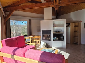 A cozy living room with a wooden ceiling, a sofa, a fireplace, and a dining area. - PRIMERA a 1st Class villa (Quillan)