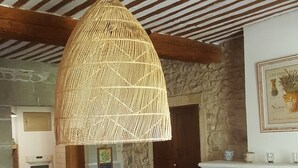 A rustic dining area with a large round table, wooden chairs, a woven pendant light, a stone wall, and a fireplace. - Mas du Coustoubi between Avignon and St Remy. Swimming pool, Pétanque, BBQ (Châteaurenard)