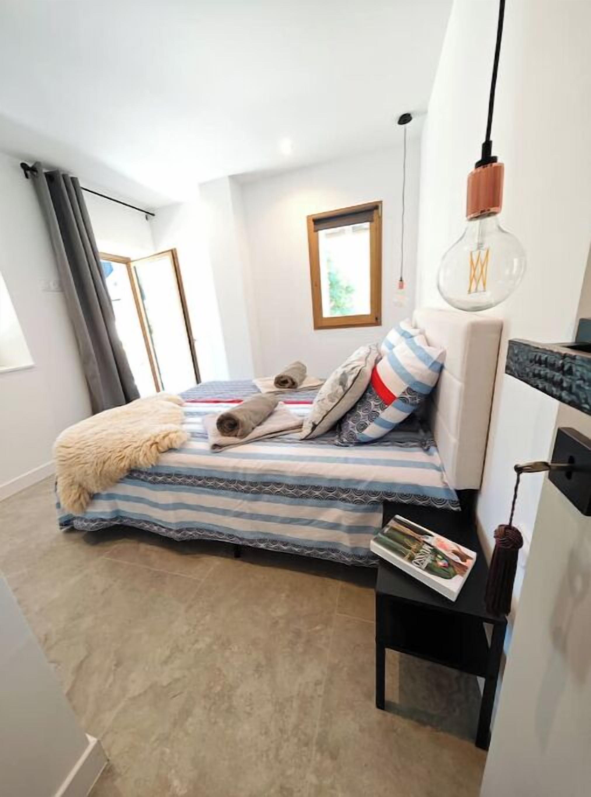 Ein kleines, modernes Schlafzimmer mit Bett, Nachttisch, Pendelleuchte und Fenster.
