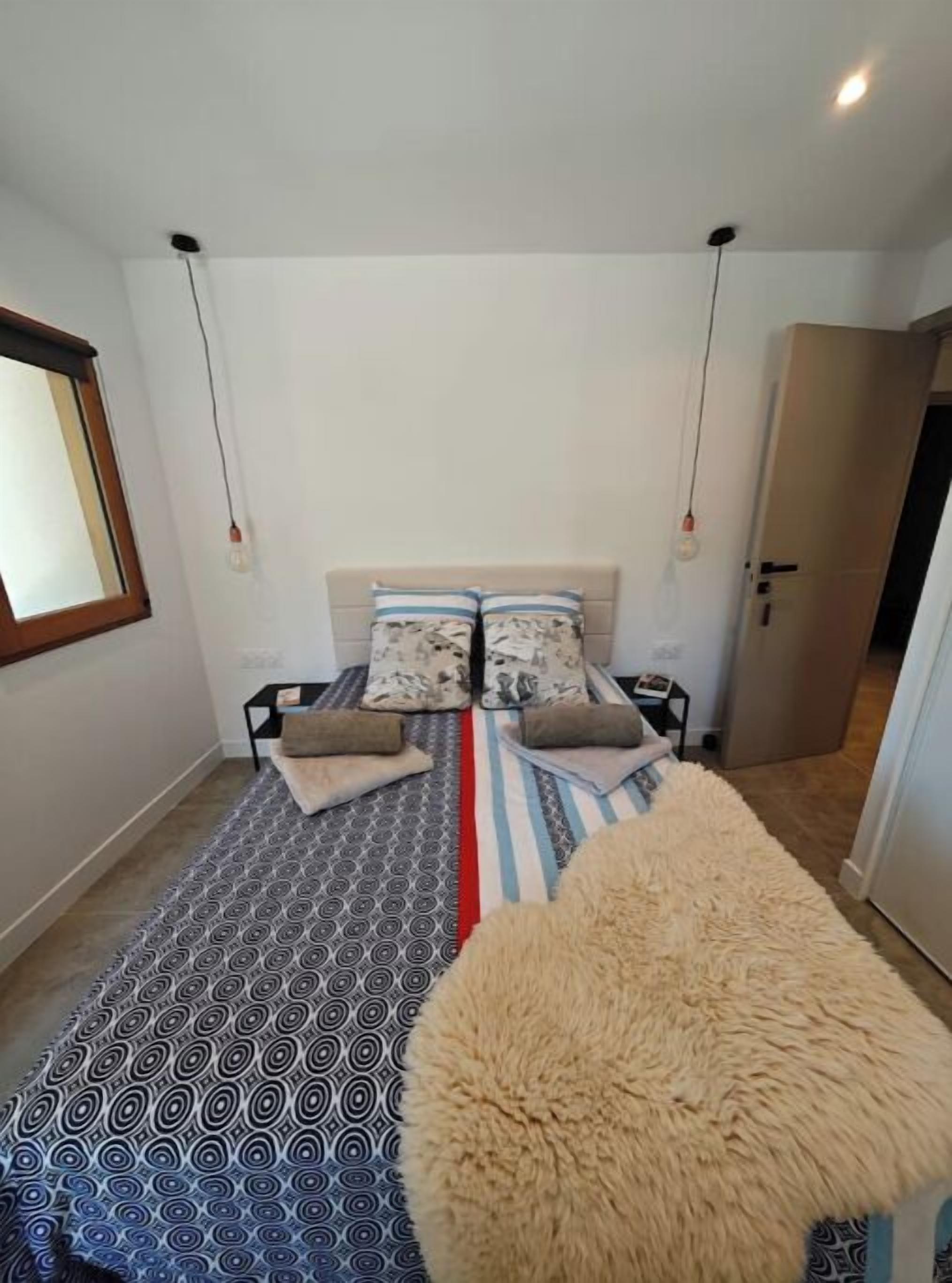 Une chambre à coucher avec une couvre-lit à motifs, deux oreillers, un tapis moelleux et une table de chevet.