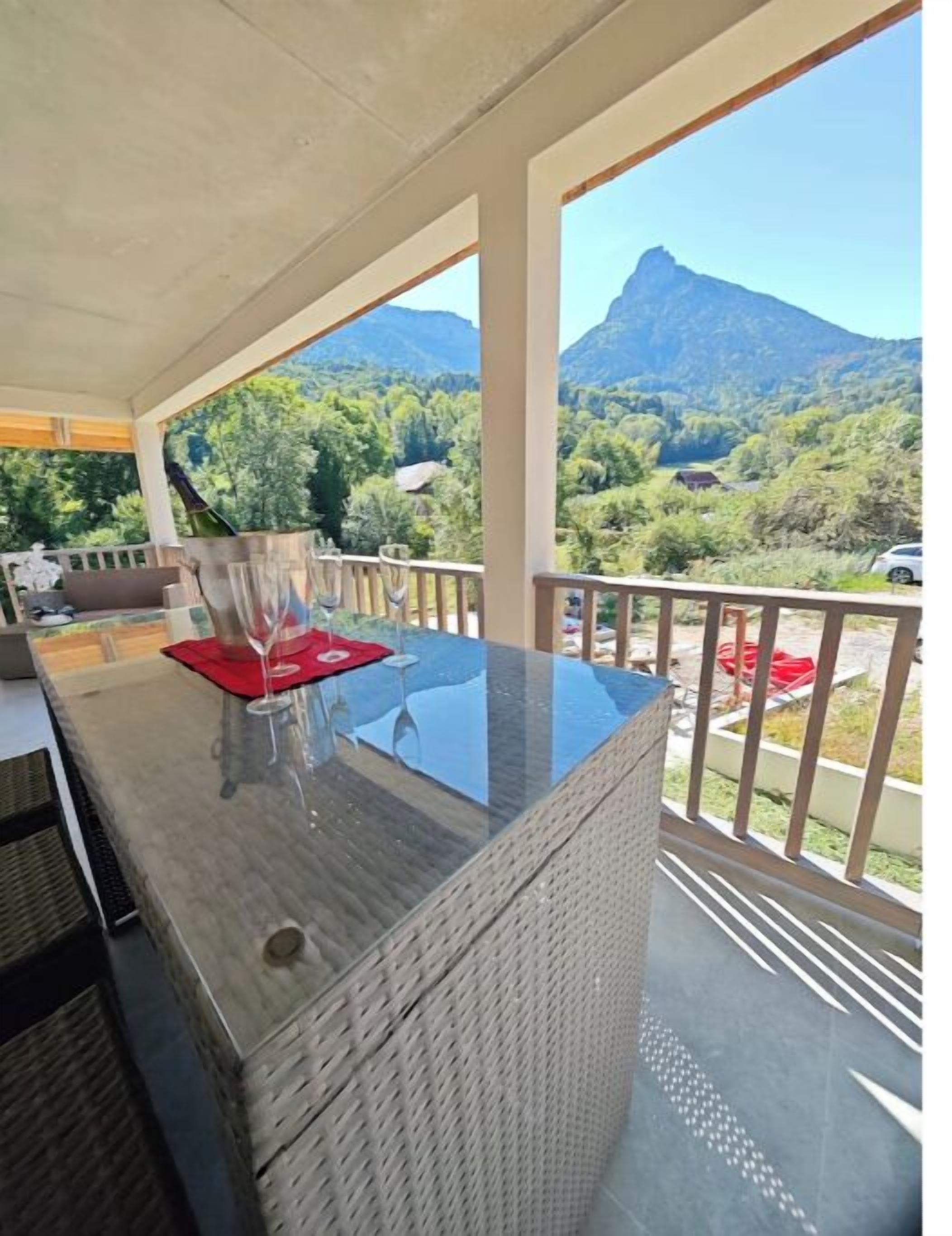 A balcony with a glass-top table, red placemat, and a bottle of wine.