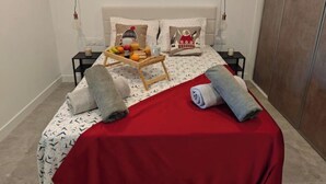 Ein ordentlich bezogenes Bett mit roter Tagesdecke, zwei Kissen und einer Obstschale.