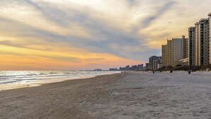 A wide sandy beach with high-rise buildings in the background. - Coastal Canopy Modern Resort Condo w Massive Pool (North Myrtle Beach)