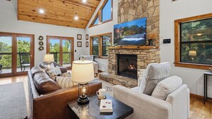 A spacious living room with a stone fireplace, a large flat-screen TV, and a cozy seating area. - Private Location, Pet Friendly, Mountain Views, Game Area, Fire Pit + Hot Tub (Gatlinburg)
