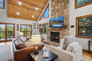 A spacious living room with a stone fireplace, a large flat-screen TV, and a cozy seating area. - Private Location, Pet Friendly, Mountain Views, Game Area, Fire Pit + Hot Tub (Gatlinburg)