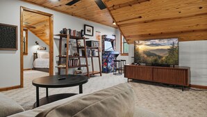 A cozy living room with a wooden ceiling, a television, a bookshelf, and a sofa. - Private Location, Pet Friendly, Mountain Views, Game Area, Fire Pit + Hot Tub (Gatlinburg)