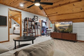 A cozy living room with a wooden ceiling, a television, a bookshelf, and a sofa. - Private Location, Pet Friendly, Mountain Views, Game Area, Fire Pit + Hot Tub (Gatlinburg)