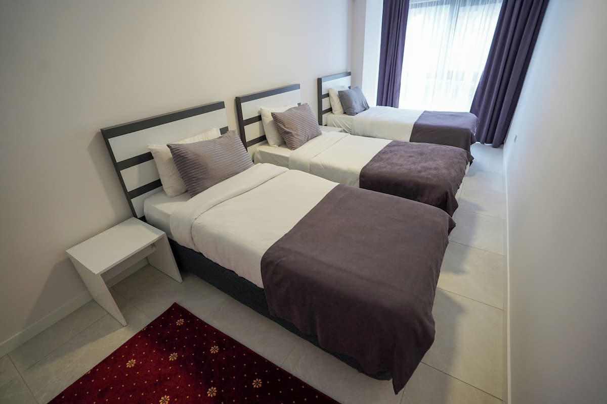 A hotel room with three beds, a small white nightstand, and a red patterned rug.