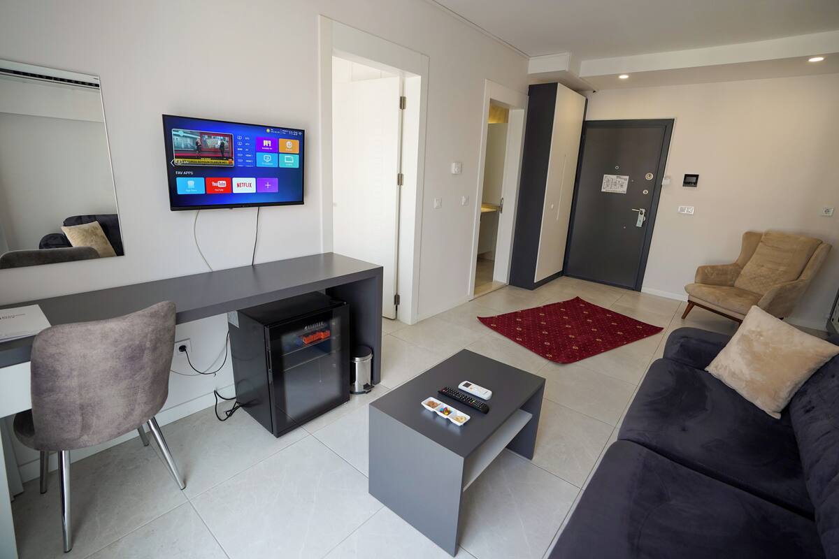 A modern living room with a flat-screen TV, a desk, a couch, and a coffee table.