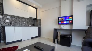 A modern living room with a flat-screen TV, a coffee table with a remote, and a small black appliance.
