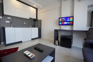A modern living room with a flat-screen TV, a coffee table with a remote, and a small black appliance.