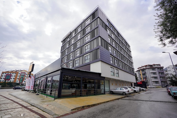 A modern building with a glass facade, multiple floors, and a parking area with cars. - elea premium stay (Denizli)