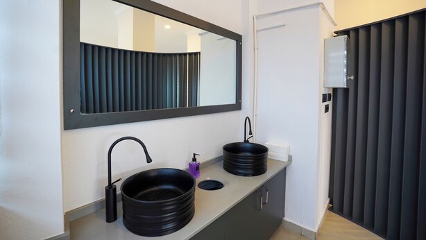A modern bathroom with two black sinks, a large mirror, and a dark-colored partition.