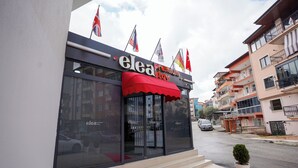 A hotel named "elea Premium Stay" with a red awning and multiple flags.