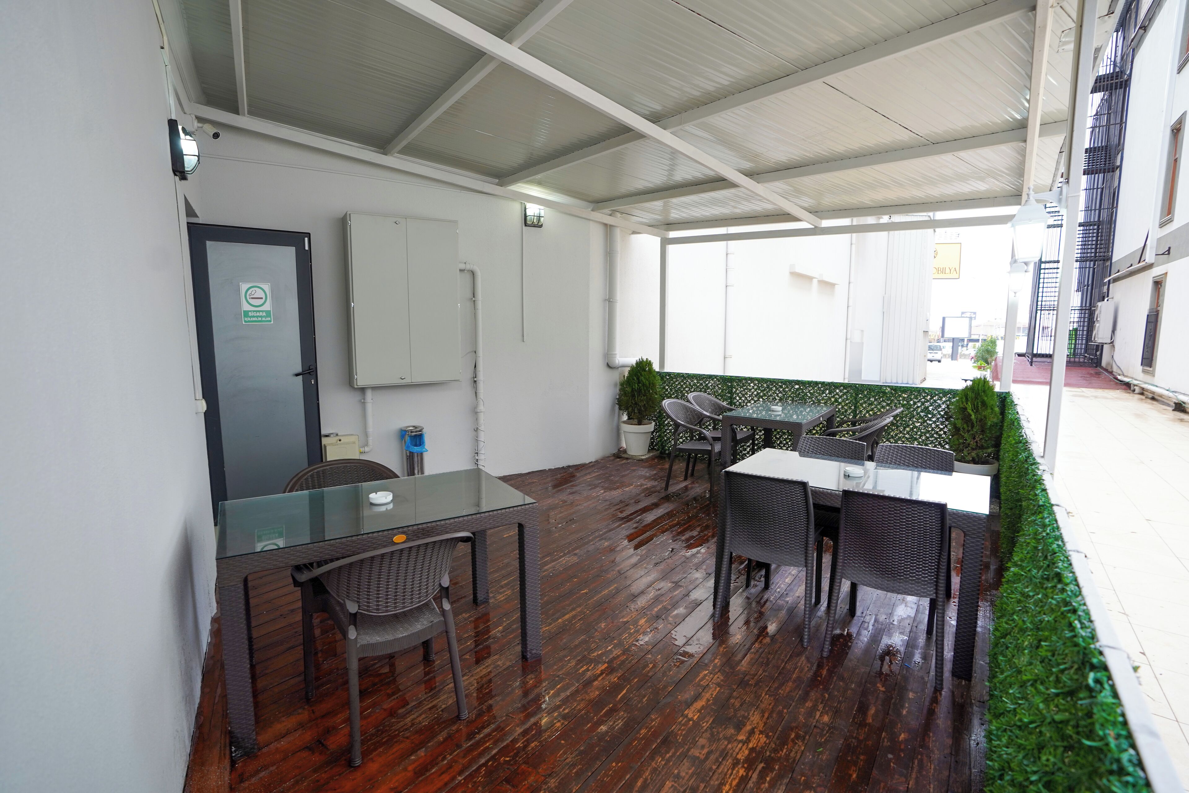 A covered outdoor area with a table and chairs, a potted plant, and a white wall with a door.