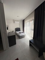 A modern bedroom with a bed, a desk, and a large window with curtains.