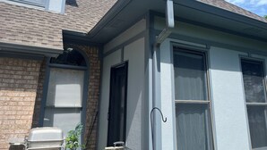 Una casa con fachada de ladrillo, una ventana con contraventanas y una reja en el porche.