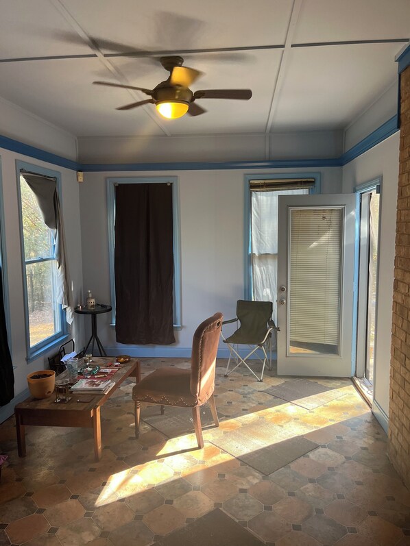 A sunlit room with a ceiling fan, a dining table with chairs, and a door leading outside.