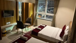 A hotel room with two beds, a TV, a chair, and a window with a city view. - Hotel Tirupati Inn (Ujjain)