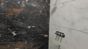 A bathroom with black and white marble tiles, a showerhead, and a blue bucket. - Hotel Tirupati Inn (Ujjain)