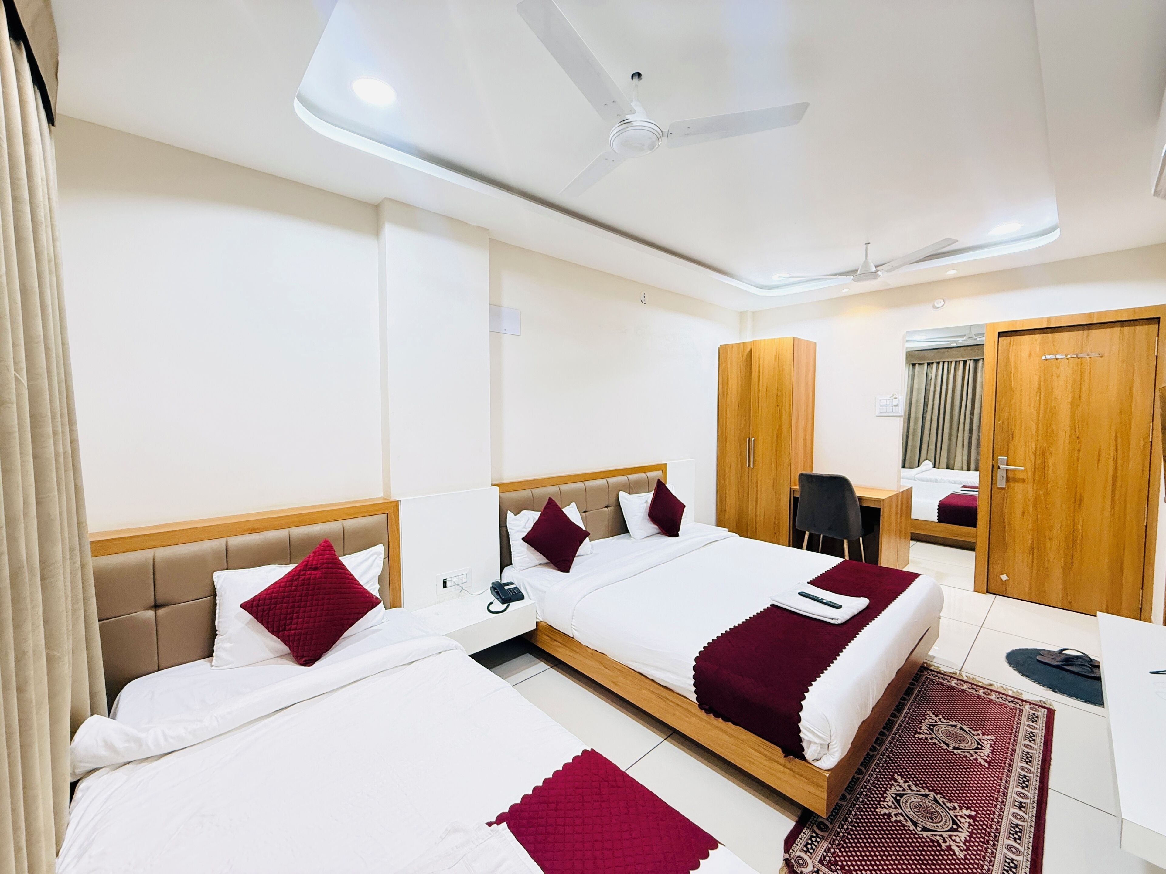 A hotel room with two beds, a desk, a wardrobe, and a ceiling fan.