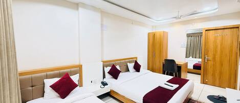 A hotel room with two beds, a desk, a wardrobe, and a ceiling fan.