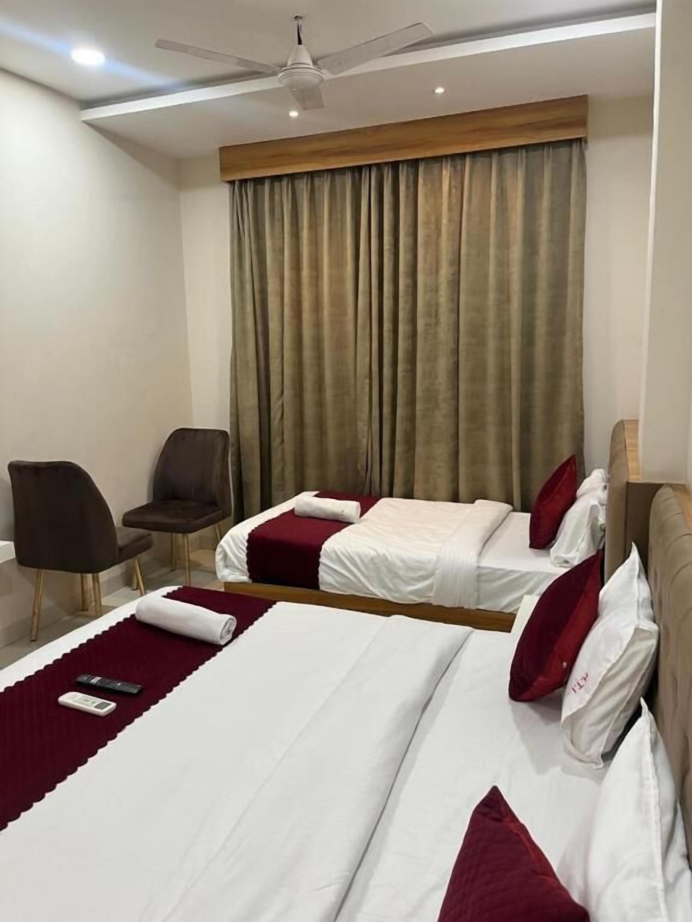 A hotel room with two beds, a ceiling fan, a chair, and a large window with curtains.
