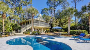 Une maison à deux étages avec une piscine, entourée d’arbres et agrémentée de mobilier d’extérieur.