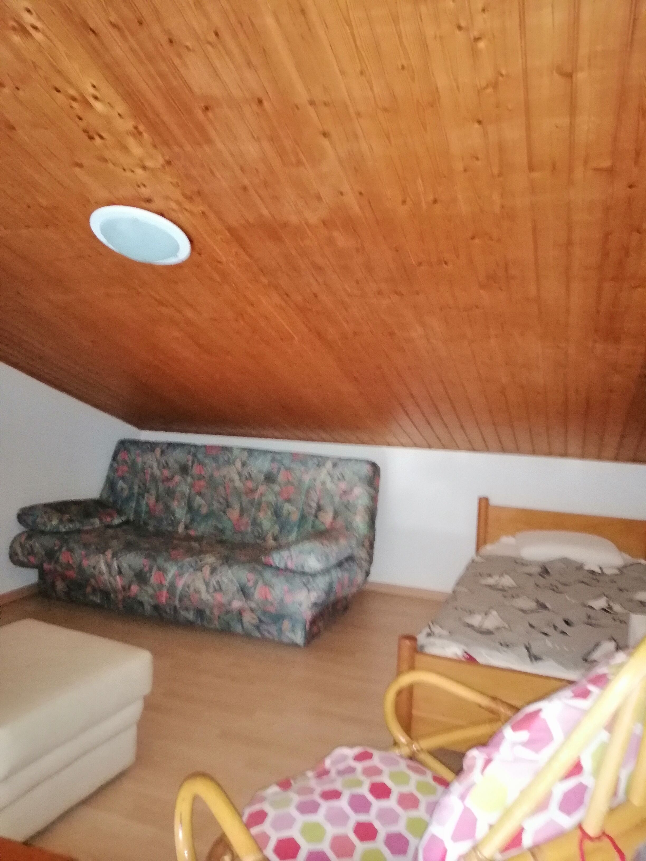 Ett litet, ombonat rum med ett träpanelat tak, en blommönstrad soffa, en säng med ett mönstrat överkast och en liten stol.