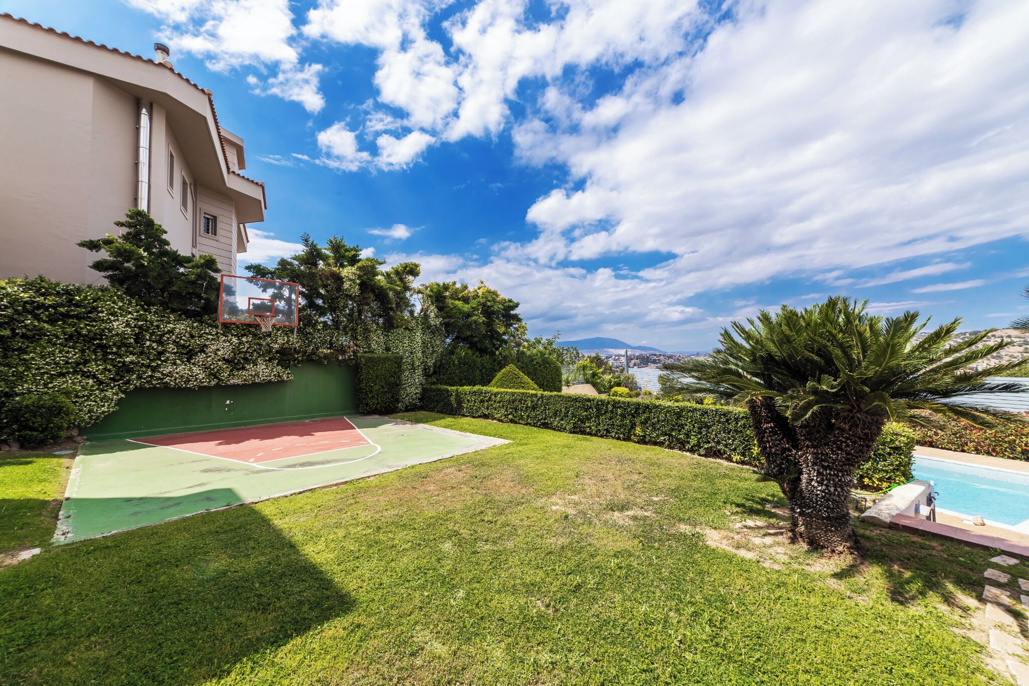 A well-maintained outdoor area with a tennis court, a swimming pool, and a view of a cityscape.