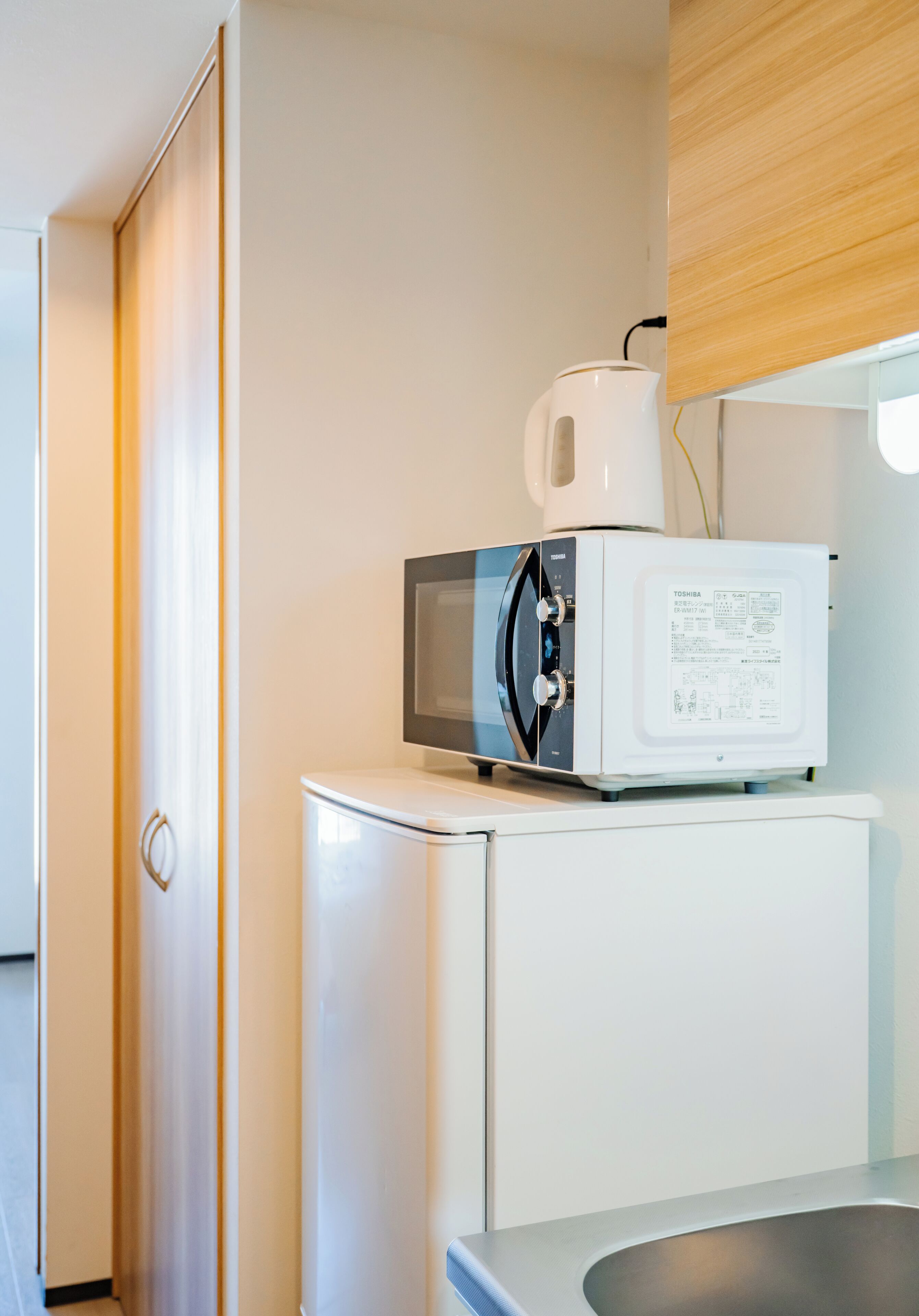 A compact kitchen with a microwave, a kettle, and a sink.