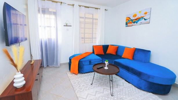 Una sala de estar con un sofá azul, una mesita, un televisor y un cuadro en la pared.