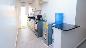 Una cocina compacta con armarios blancos, cocina a gas, refrigerador y dispensador de agua azul.