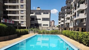 Una piscina con un borde de baldosas, rodeada de edificios residenciales de baja altura.