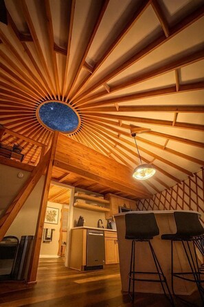 A kitchen with wooden beams, a bar area with stools, and a ceiling with a circular skylight. - Modern Forest Yurt with Firepit & Skylit Dome near Carson, Washington (Carson)