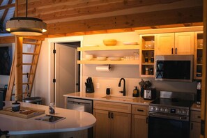 A compact kitchen with wooden cabinets, a microwave, a stove, and a sink. - Modern Forest Yurt with Firepit & Skylit Dome near Carson, Washington (Carson)