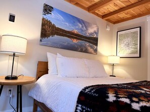 Een slaapkamer met een bed, twee bedlampen, een schilderij van een berglandschap en een kaart in een lijst aan de muur.