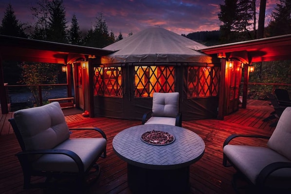 An outdoor patio with a round table and four chairs, a covered seating area with a view of the landscape, and a wooden deck.