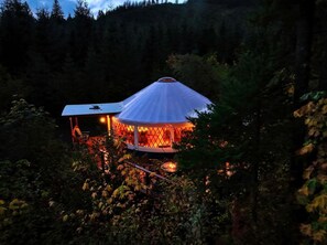 Une tente en forme de dôme, avec un feu allumé à l’intérieur, entourée d’une forêt dense.