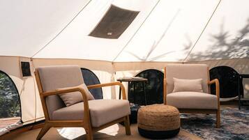 A tent with two wooden chairs, a round ottoman, and a small table.