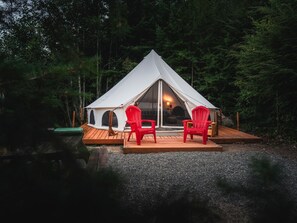 Une tente avec une terrasse en bois et deux chaises rouges.