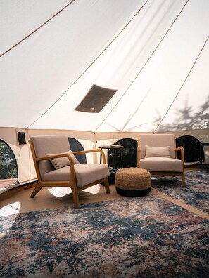 Une tente avec deux chaises en bois, un pouf rond et une petite table.