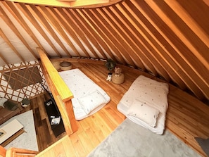 An attic bedroom with wooden slats, two beds with patterned bedding, a small statue, and a wicker basket.