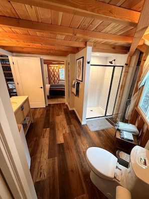 Un baño pequeño y acogedor, con paneles de madera, ducha, inodoro y una mesita de noche.
