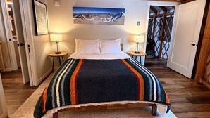 A bed with a striped blanket, two bedside lamps, a framed picture on the wall, and wooden beams on the ceiling. - Modern Luxury Yurt with Firepit Table & Skylit Dome near Carson, Washington (Carson)