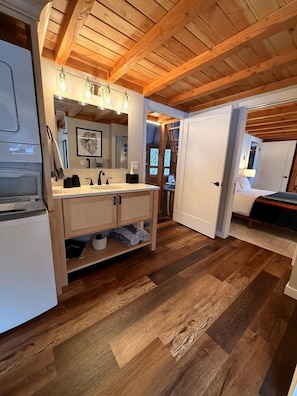 A modern bathroom with wooden beams, a sink, mirror, and a shower area.