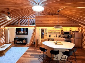 Un interior estilo loft con una isla central, vigas de madera, un televisor, electrodomésticos de cocina y una escalera.